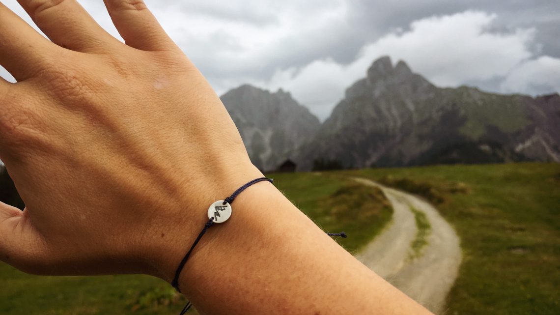 Eine Hand mit einem Bergarmband vor Berge