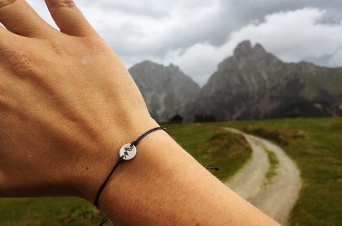 Eine Hand mit einem Bergarmband vor Berge